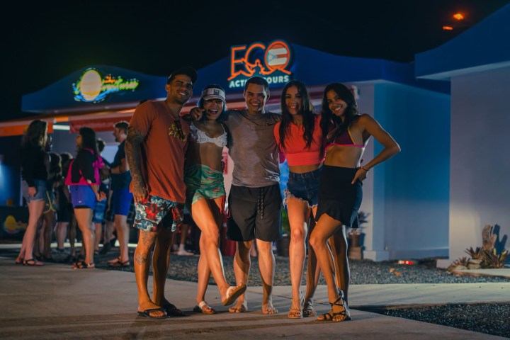 Group of five friends smiling outside a building at night.