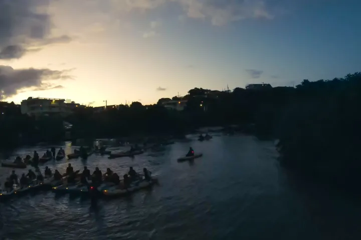 Group kayaking at dusk on a calm river with a sunset in the background.