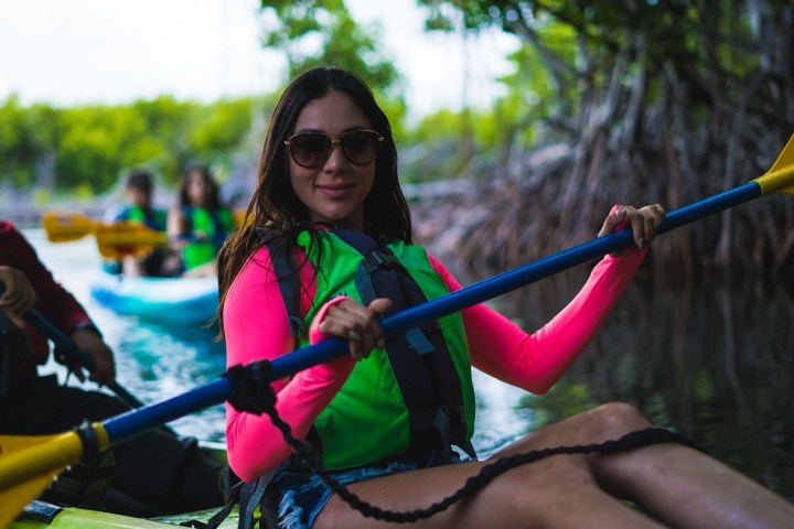 Woman in bright pink sleeves kayaking in a mangrove forest with others.