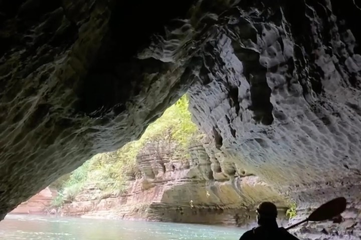 Person kayaking inside a rocky cave with light visible outside.