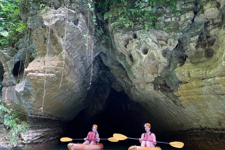 Two people kayaking in turquoise water outside a cave entrance.