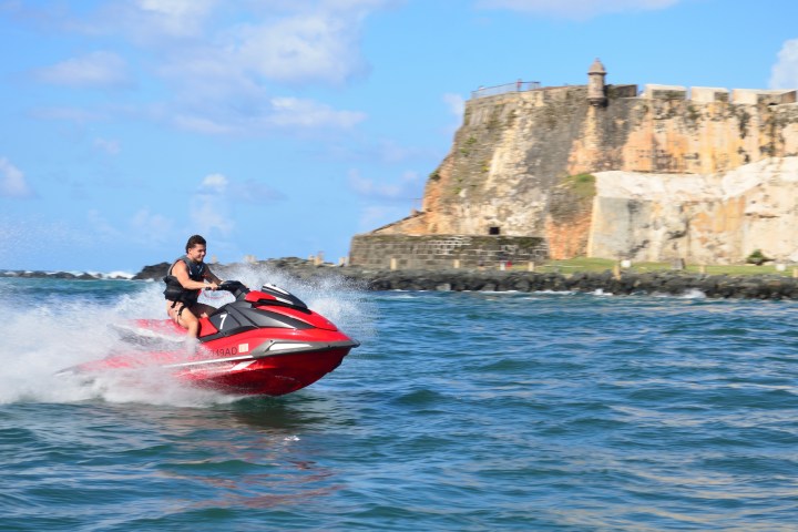 Person riding a red jet ski near a historic fort on a sunny day.